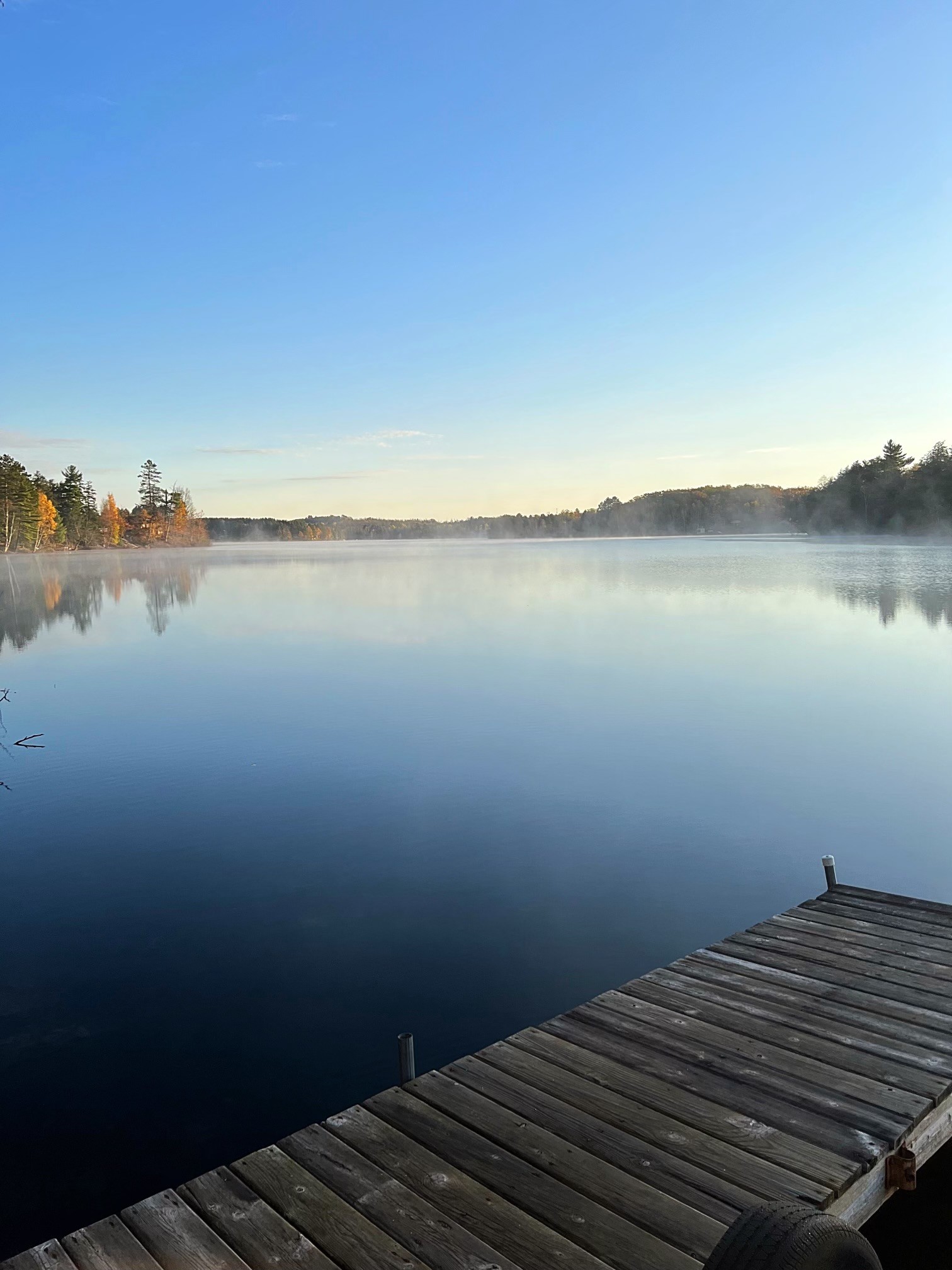 Fog rising off a calm lake at dawn with a wooden dock in the foreground